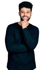 Young arab man with beard wearing casual winter sweater smiling looking confident at the camera with crossed arms and hand on chin. thinking positive.