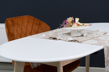 White wooden table combined with orange wooden chairs with soft fabric upholstery. There is a white delivery with a multi-colored bouquet of flowers on the table