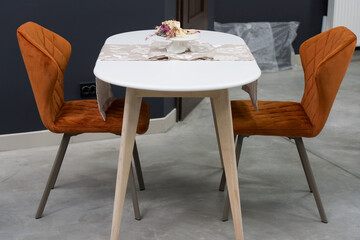 White wooden table combined with orange wooden chairs with soft fabric upholstery. There is a white...