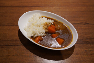 Japanese curry with rice in a white plate on a wooden table