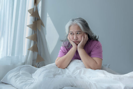 Elderly Asian woman sleeping on white bed having headache because it is pressure related disease and migraine to retirement and health care concept.