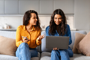 Two women using a laptop on a sofa