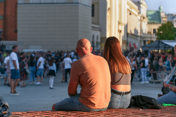 Amidst the hustle and bustle of the city, a young man and a girl sit side by side at sunset,...