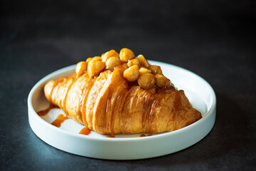 Plate of tasty croissant with chocolate and almond on dark wooden table. French pastry.