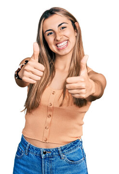 Hispanic young woman wearing casual summer shirt approving doing positive gesture with hand, thumbs up smiling and happy for success. winner gesture.