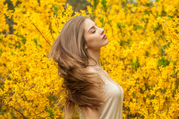 Spring fashion model with long brown hair and natural makeup against floral background outdoor