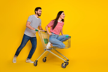 Full length photo of positive couple wear t-shirt sit in cart look at discount ride in empty space...