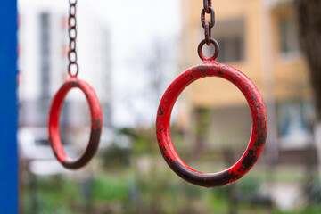 Street old metal gymnastic rings of red color with peeling paint