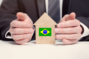 Businessman hand holding wooden Home model with Brazilian flag. insurance and property concepts