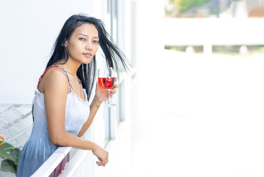 A woman in a summer dress holds a full wine glass in the balcony of a residential building