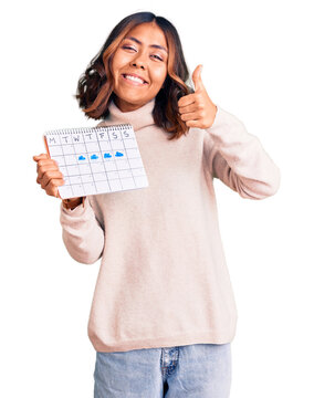 Young beautiful mixed race woman holding travel calendar smiling happy and positive, thumb up doing excellent and approval sign