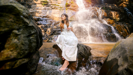 beautiful asian woman wearing white dress standing in front of waterfall in natural park