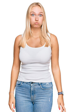 Young blonde girl wearing casual style with sleeveless shirt puffing cheeks with funny face. mouth inflated with air, crazy expression.