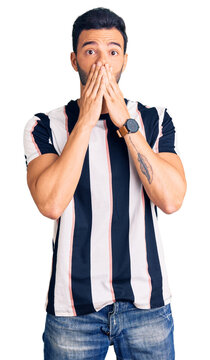 Young handsome hispanic man wearing striped tshirt shocked covering mouth with hands for mistake. secret concept.