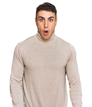 Hispanic young man wearing casual turtleneck sweater scared and amazed with open mouth for surprise, disbelief face