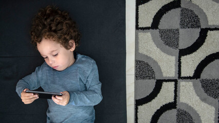 Criança com cabelos cacheados com expressão pensativa brincando de jogos no celular, pensativo,...