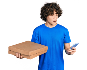 Caucasian teenager holding delivery package and showing smartphone screen in shock face, looking skeptical and sarcastic, surprised with open mouth
