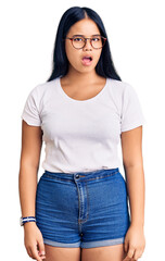 Young beautiful asian girl wearing casual clothes and glasses in shock face, looking skeptical and sarcastic, surprised with open mouth