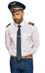 Handsome man with beard wearing airplane pilot uniform skeptic and nervous, frowning upset because...