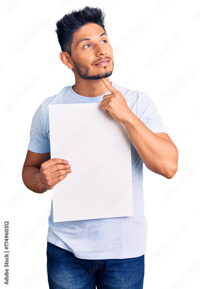 Wall mural handsome latin american young man holding cardboard banner with blank space serious face thinking ab