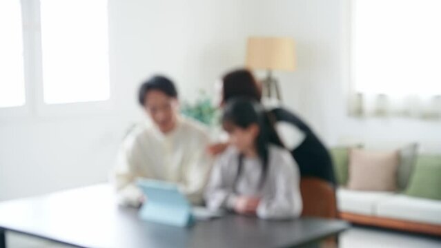 Blurred concept of family of an Asian girl and her parents looking at a tablet PC screen.