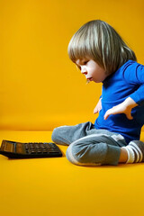 A small child counts on a calculator on a yellow background. Kid fingers press buttons and...