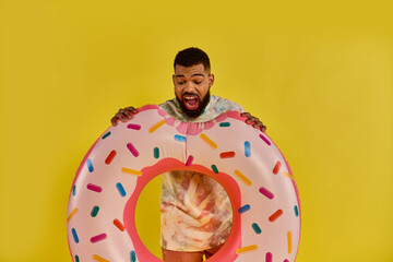 A man with a smile on his face holding a massive donut covered in colorful sprinkles, showcasing a...