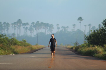 homem caminhando em rodovia em Calçoene, Amapá, em amanhecer com neblina  - obrazy, fototapety, plakaty
