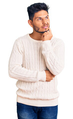 Fototapeta premium Handsome latin american young man wearing casual winter sweater serious face thinking about question with hand on chin, thoughtful about confusing idea