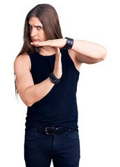 Young adult man with long hair wearing goth style with black clothes doing time out gesture with...