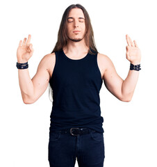 Young adult man with long hair wearing rocker style with black clothes and contact lenses relax and smiling with eyes closed doing meditation gesture with fingers. yoga concept.