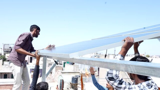 Indian workers installing solar panels on roof of house. Maintenance of photovoltaic panel system. Concept of alternative, renewable energy.