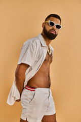A fashionable man in white shorts and stylish sunglasses is confidently posing for a picture,...