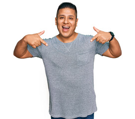 Young latin man wearing casual clothes looking confident with smile on face, pointing oneself with...