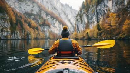 rear view of a man on a kayak floating on a serene mountain lake surrounded by steep cliffs and forest in autumn - obrazy, fototapety, plakaty