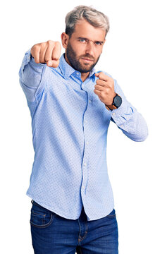 Young handsome blond man wearing elegant shirt punching fist to fight, aggressive and angry attack, threat and violence