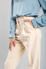 Elegant woman in pleated beige pants and blue blouse with hand in pocket