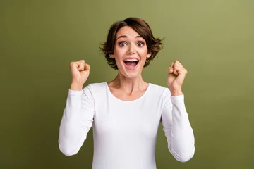 Poster Portrait of funny overjoyed lady holding raised fists open mouth big win lottery money isolated khaki green color background © deagreez