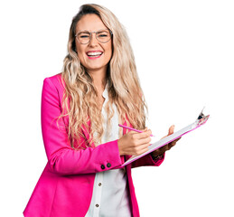 Young blonde woman writing on clipboard smiling and laughing hard out loud because funny crazy joke.