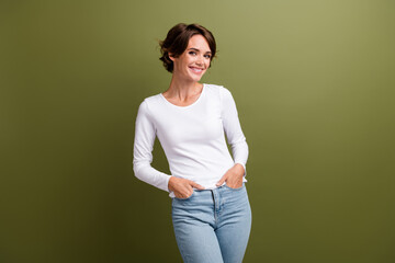 Portrait of young adorable lady holding arms in pockets denim pants posing good mood isolated khaki green color background