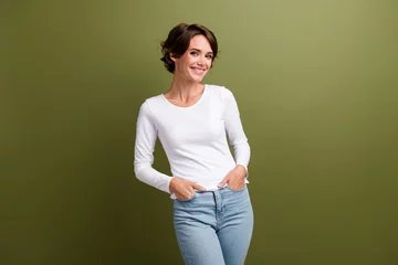 Tuinposter Portrait of young adorable lady holding arms in pockets denim pants posing good mood isolated khaki green color background © deagreez