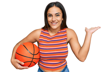 Young brunette woman holding basketball ball celebrating victory with happy smile and winner expression with raised hands