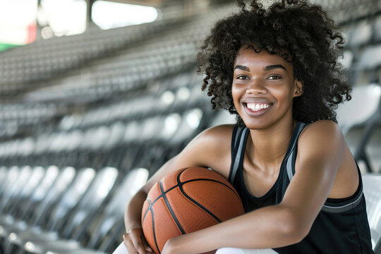 An African American female basket player sitting on the stadium stands, smiling woman holding a basketball, embodying the concept of passion for the sport, game and physical training