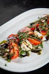 Traditional italian food - caprese salad with mozzarella cheese, tomatoes and pesto sauce. Caprese salad on black concrete background in minimal style. Italian appetizer caprese on dark background