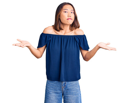 Young beautiful chinese girl wearing casual clothes clueless and confused expression with arms and hands raised. doubt concept.