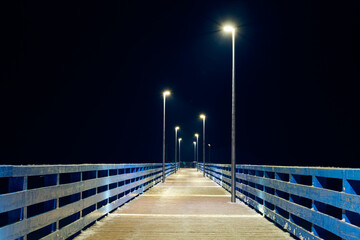 Lampposts along pier going into night darkness above sea symbolize serene scene of calmness cold...