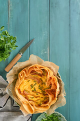 Homemade quiche or tart with slices of bacon and leeks with tortilla instead of dough on wooden cutting board on rustic old wooden background. Quiche open tart traditional French cuisine. Top view.