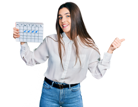 Young brunette teenager holding travel calendar pointing thumb up to the side smiling happy with open mouth