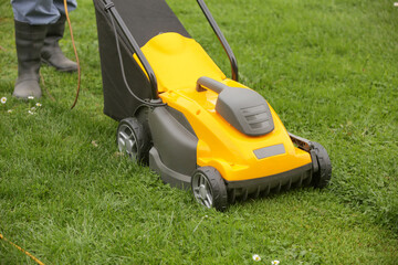Gardener in black rubber boots trimming lawn with mower