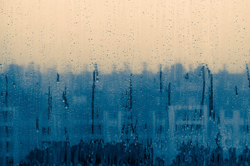 A blurry image of a city skyline with a blue and white background. The image has a moody and dreamy feel to it, as if the viewer is looking through a foggy window